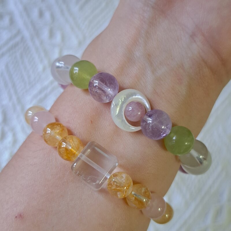 Two crystal bead bracelets stacked on one wrist, with citrine, rose quartz, clear quartz and amethyst beads