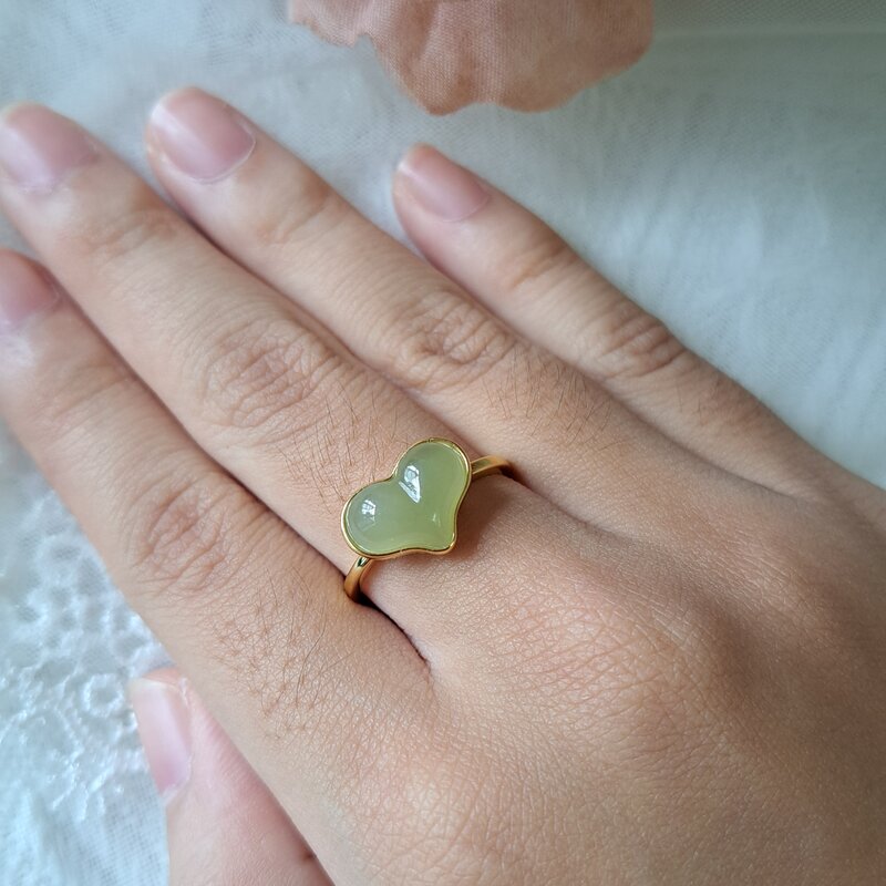 A heart-shaped pale green jade ring worn on a hand, against white lace